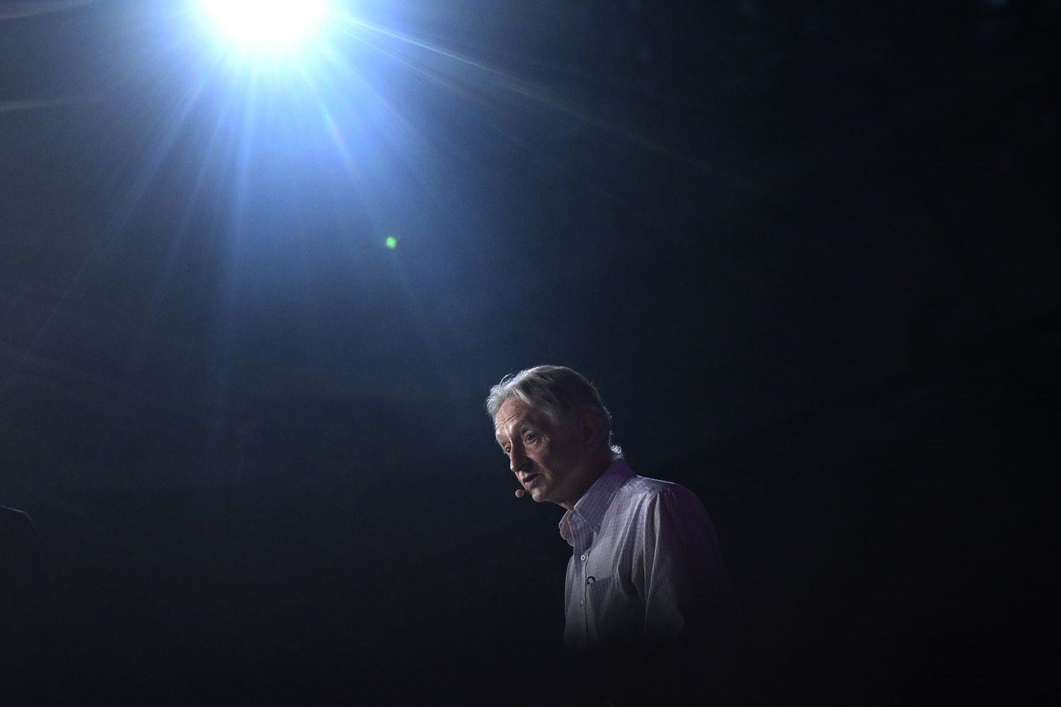 Geoffrey Hinton speaks at an event with a spotlight shining on him against a dark background.